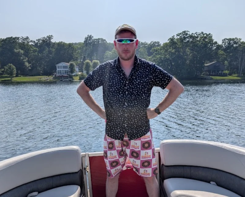 Sam standing on a pontoon boat in Dunkin' print swim trunks